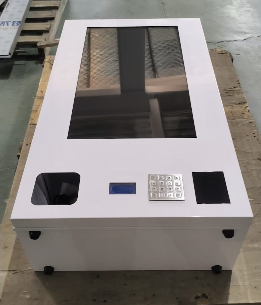 Assembled wall-mount vending machine on the factory floor, showing the 32-inch screen, metal keypad, coin slot and contactless reader