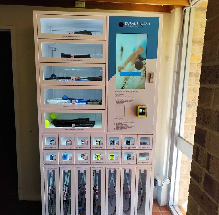 Rental and hire kiosk in service at a racquet-sports club, with racquets in the hire compartments and balls in the retail cells