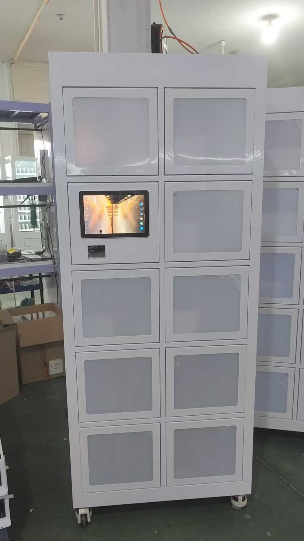 White ten-compartment KioskForce delivery locker on castors, each cell door carrying a translucent panel, with a touchscreen and QR scanner set into the second row and an identical second cabinet standing behind it