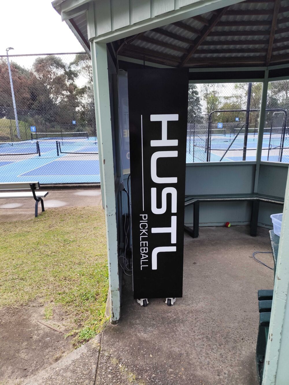 Pickleball hire locker installed on castors inside an open-sided shelter beside outdoor courts