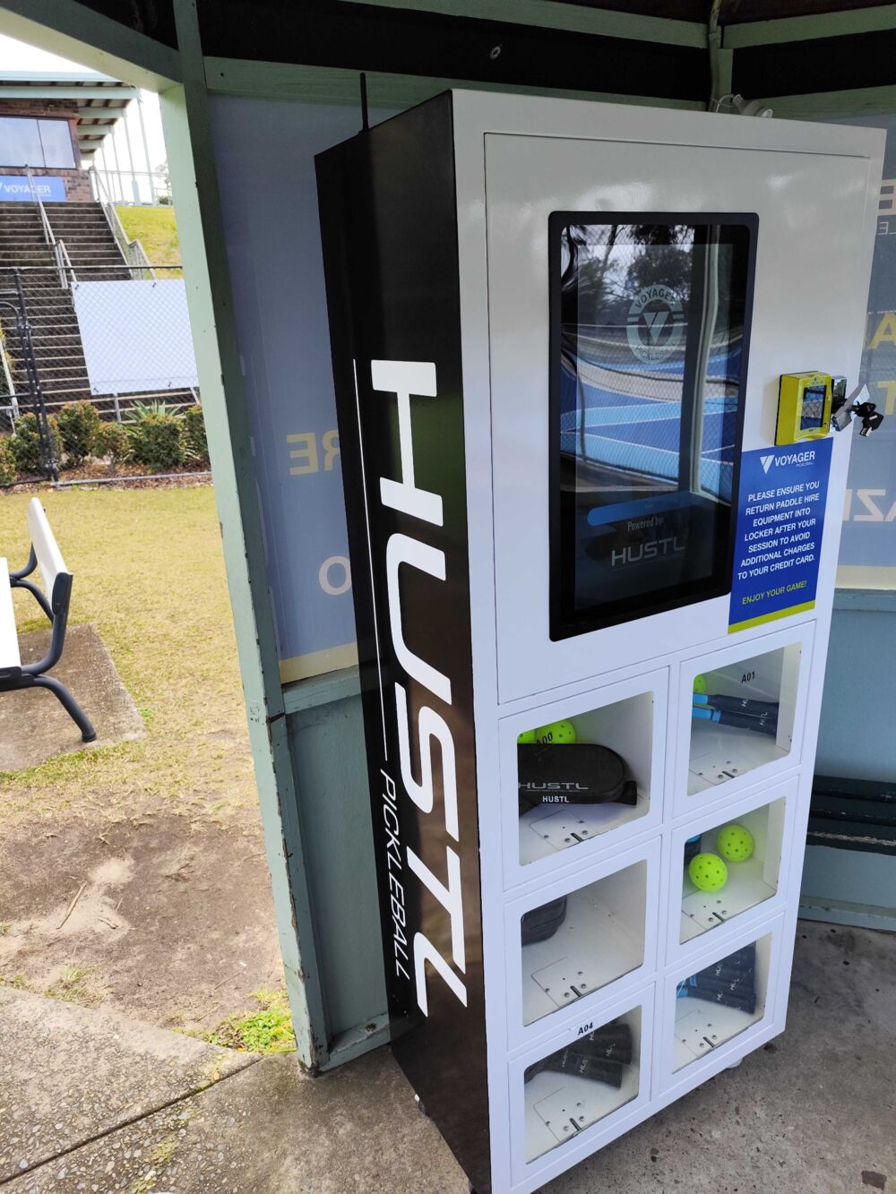 Pickleball paddle hire locker with paddles and balls loaded behind glazed compartment doors, touchscreen above and contactless card reader alongside