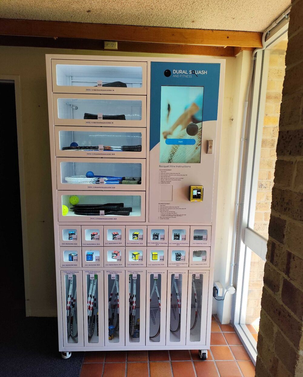 Racquet-sports hire locker at an indoor club with tall racquet compartments and small retail cells for balls